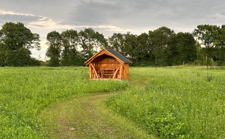 Sitzhütte Quarnstedt Holzhütte in einem grünen Feld unter bewölktem Himmel.