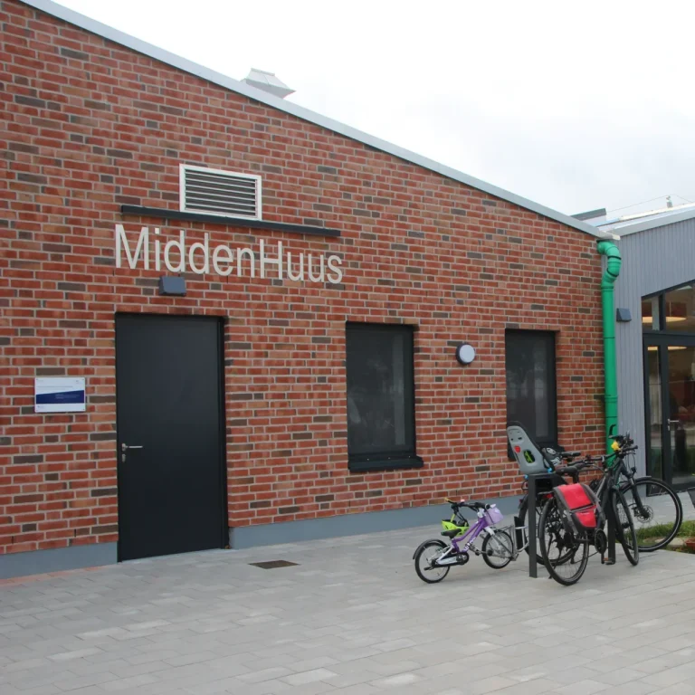 Gebäude mit roter Backsteinfassade, beschriftet "MiddenHuus", Fahrräder davor.