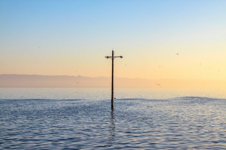 Ein einzelnes Kreuz ragt aus ruhigem Wasser bei Sonnenaufgang.