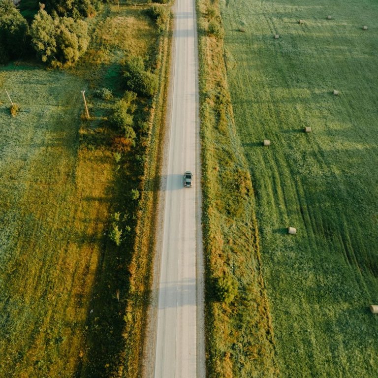 Eine einsame Straße verläuft zwischen grünen Wiesen und Bäumen.