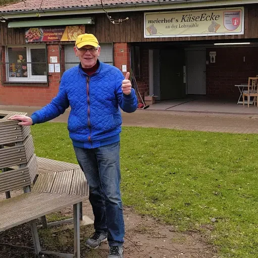 Mann mit gelber Mütze und blauer Jacke steht vor einem Restaurant.