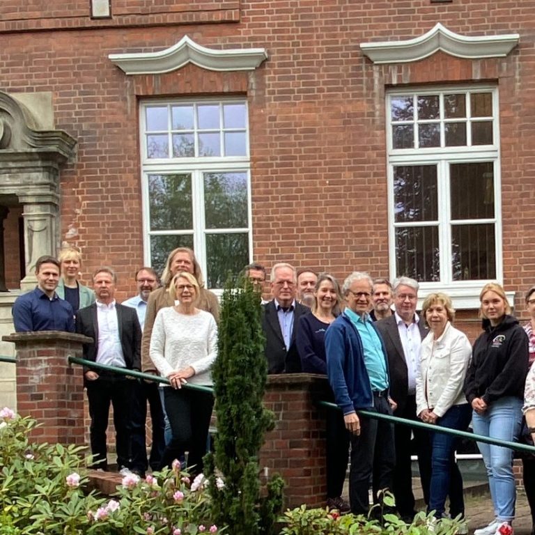 Gruppe von Menschen posiert vor einem historischen Gebäude mit Blumenbeeten.