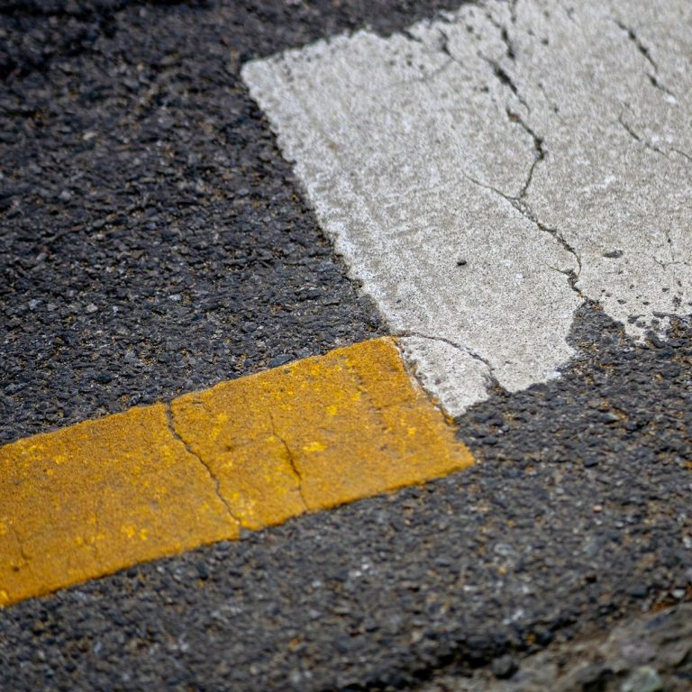 Nahaufnahme einer Straßenmarkierung mit gelbem und weißem Farbabschnitt auf Asphalt.