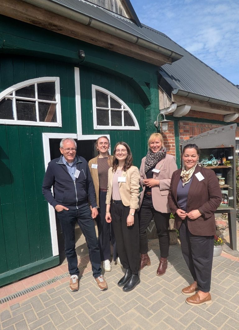 Fünf Menschen posieren vor einem grünen Eingang eines Gebäudes im Freien.