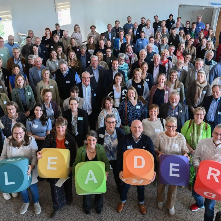 Gruppenvorstellung mit Menschen, die große bunte Buchstaben "LEADER" halten.