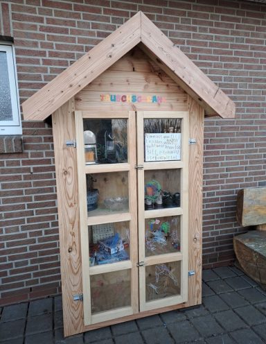 Ein kleiner Holzschrank mit Fenstern, gefüllt mit bunten Spielsachen.