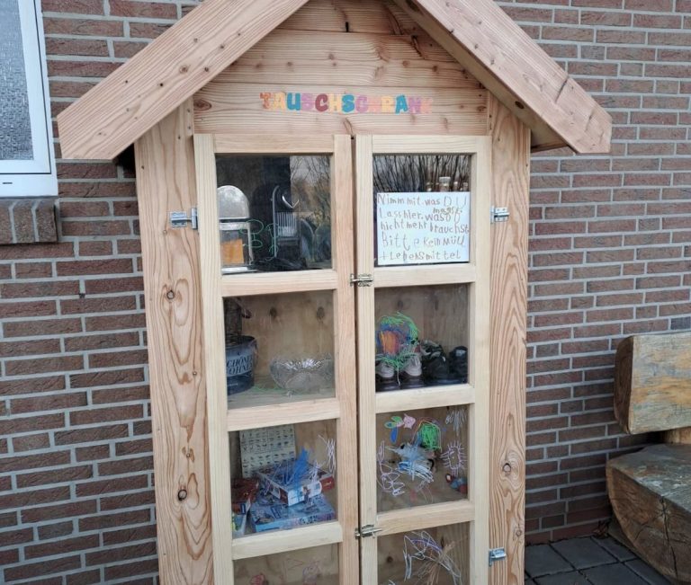 Holzhaus mit Glastüren, gefüllt mit verschiedenen Gegenständen und einem Hinweis.