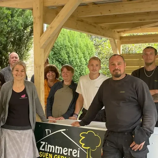 Gruppe von Handwerkern lächelt am Eingang einer Zimmerei unter einem Holzbau.