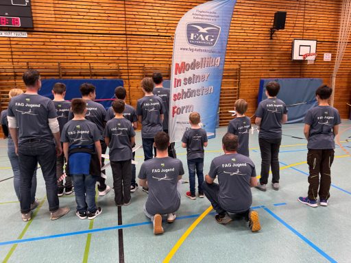Vereinsmitglieder in grauen T-Shirts stehen in einer Turnhalle vor einem Banner.