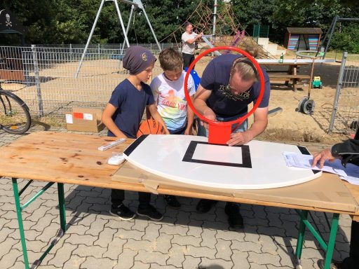 Kinder beobachten einen Mann, der an einem Tisch im Freien an einem Basketballkorb arbeitet.