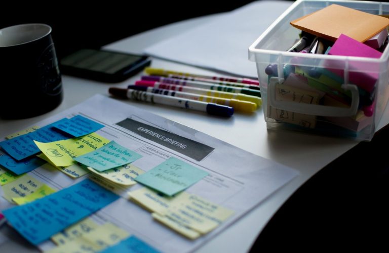 Ein Tisch mit Notizzetteln, Stiften, einem Kalender und einer Box voller Bürobedarf.