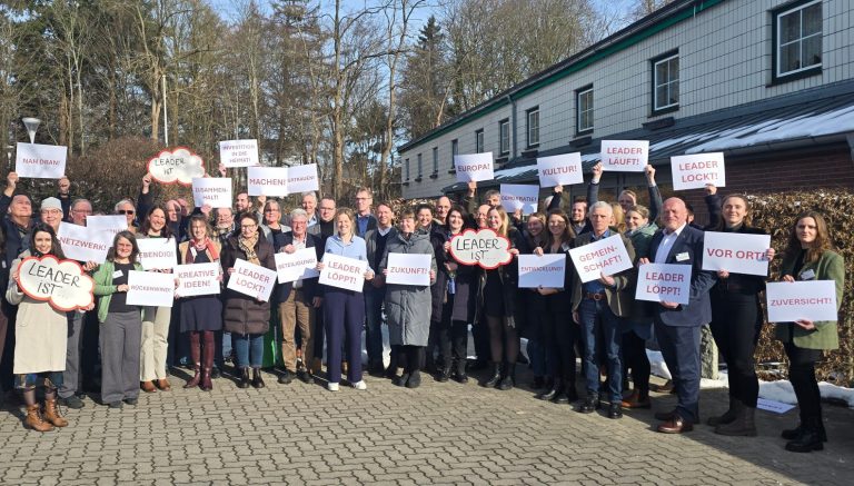 Fünf Menschen posieren vor einem grünen Eingang eines Gebäudes im Freien.