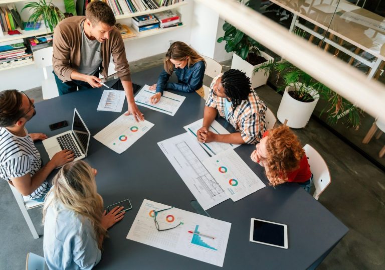 Gruppentreffen mit sechs Personen, die an einem Tisch über Diagramme diskutieren.