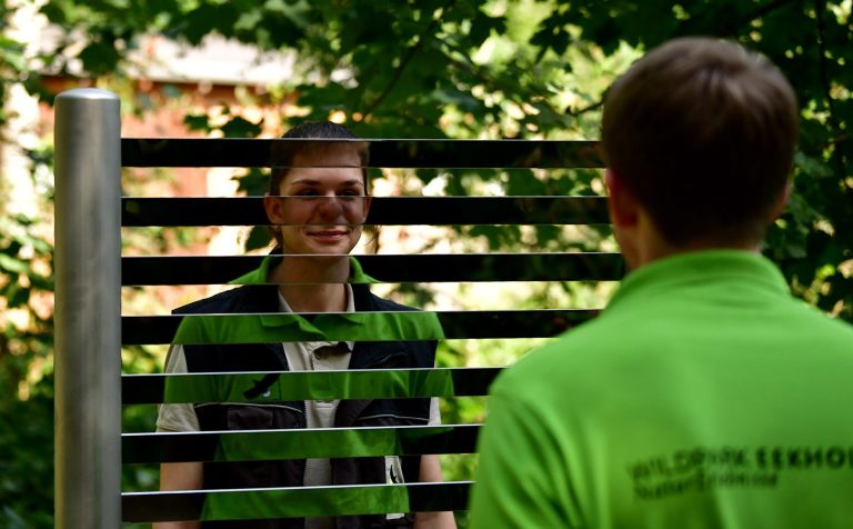 Sinneserfahrung Wildpark Eekholt Zwei Personen stehen sich gegenüber, eine lächelt, umgeben von grüner Natur.